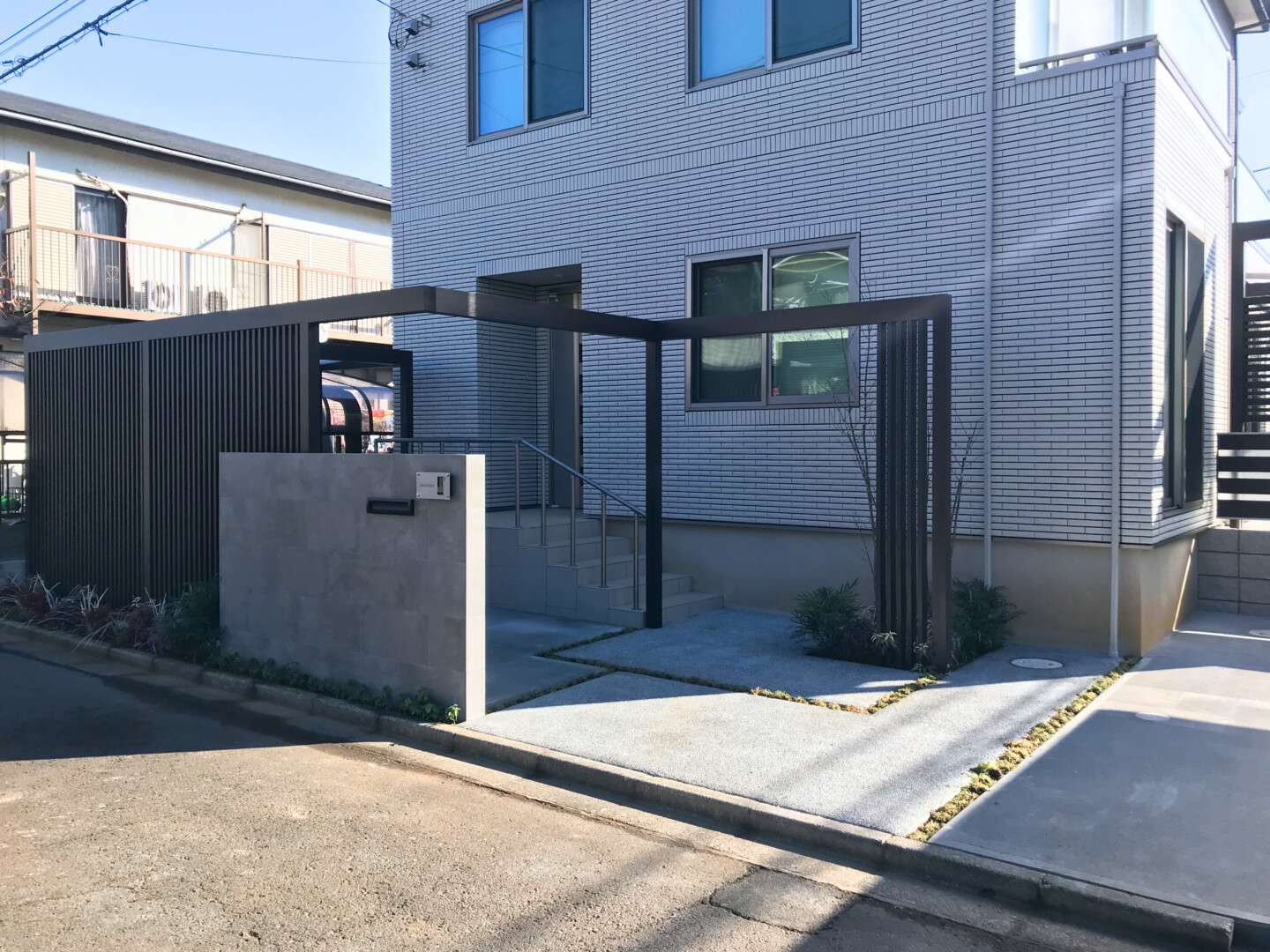 縦格子スクリーンで玄関前のプライバシーを確保しつつ、立体的な奥行きを生み出すプラスGのL字フレームと植栽の彩り