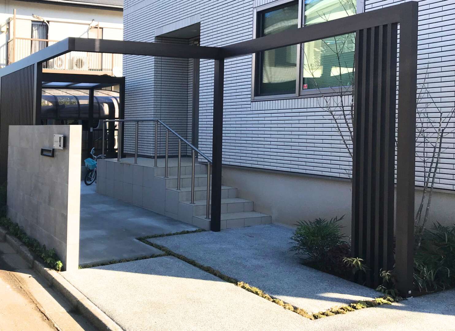 存在感のある大判タイル門柱と、スクリーンの背後に隠れるように配置された利便性の高いサイクルポート（自転車置き場）