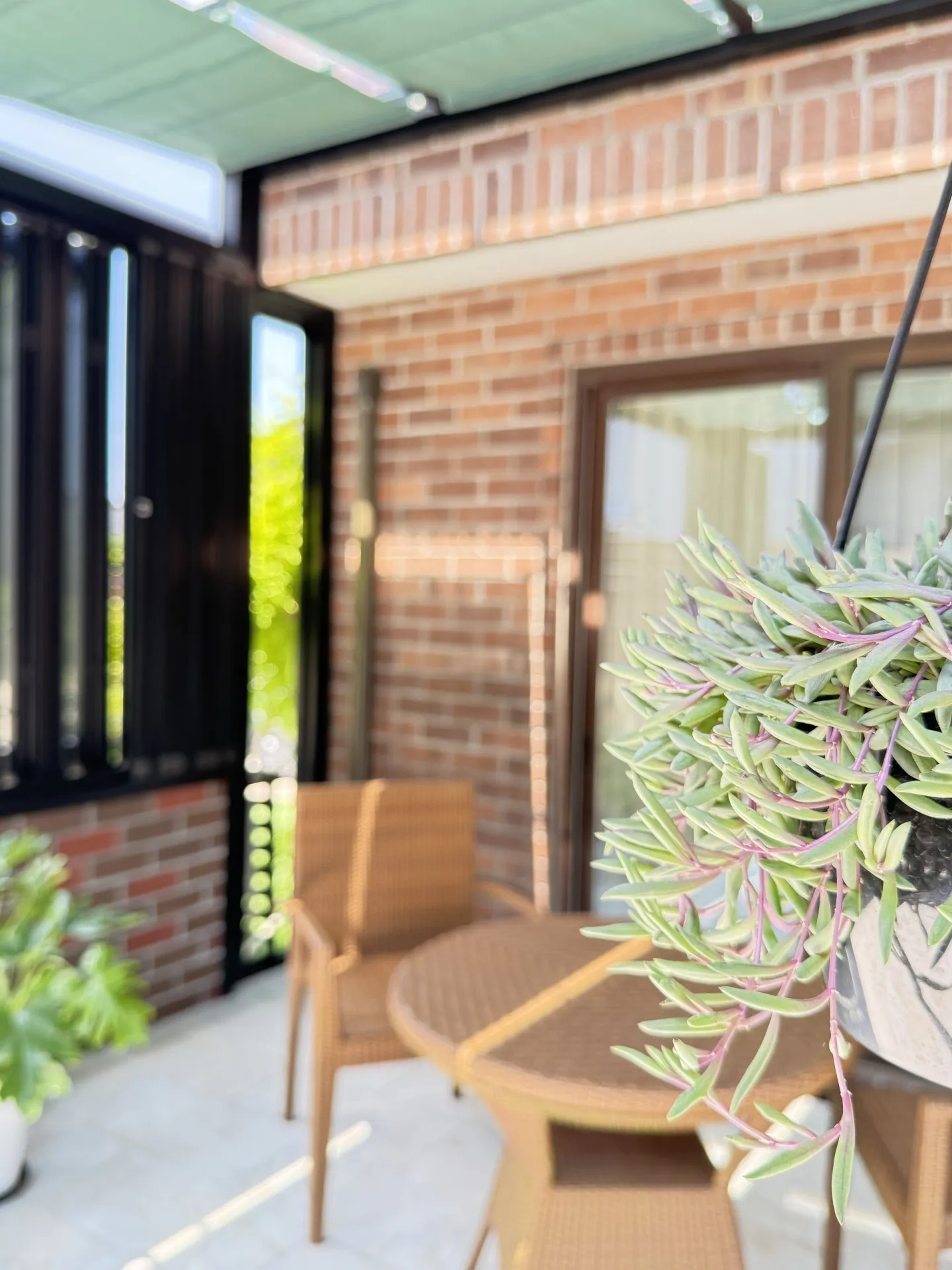 観葉植物と籐家具を配した、レンガの腰壁が印象的なガーデンルーム内観